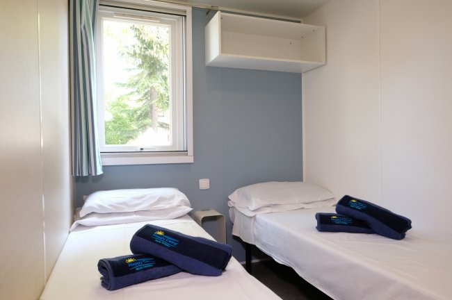 Stanza con due letti singoli, finestra, e asciugamani blu su ciascun letto.