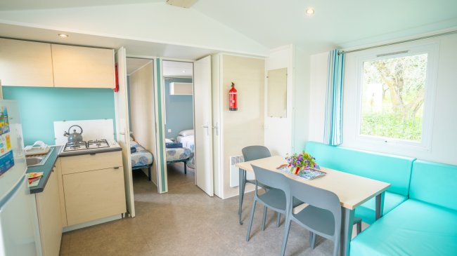 Cucina e zona pranzo luminosa con tavolo, sedie, e vista su due camere da letto aperte.