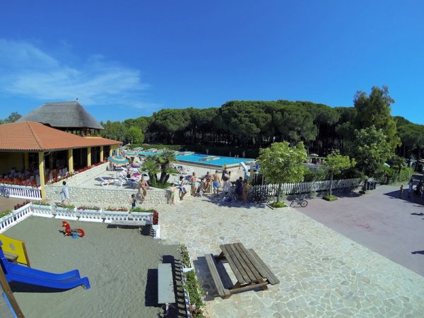 Area con piscina, parco giochi, e tavoli all'aperto, circondata da vegetazione.