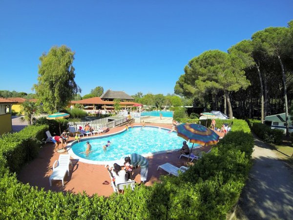 Piscina all'aperto con persone su sdraio, alberi circostanti.