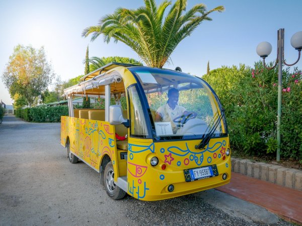 Un veicolo giallo decorato con disegni colorati, parcheggiato vicino a palme lungo una strada.