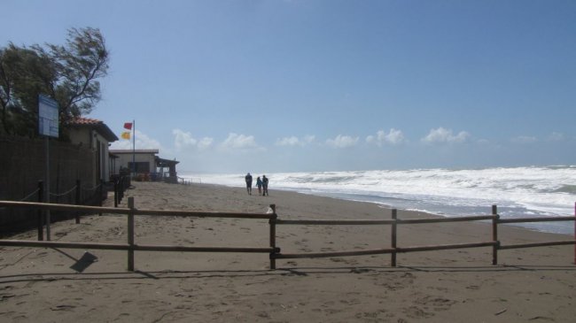 Spiaggia sabbiosa con persone che camminano, cielo limpido e onde in lontananza.