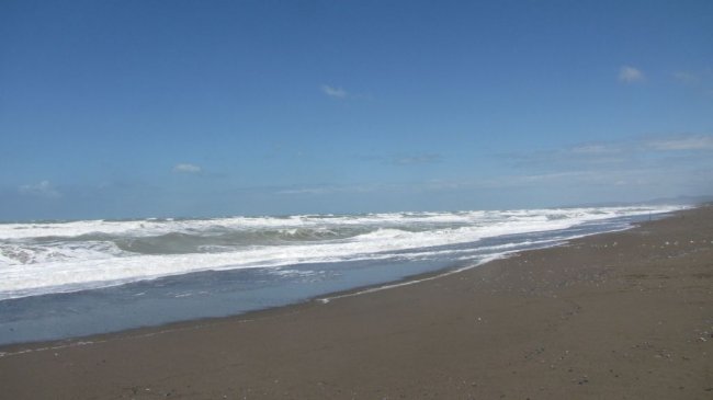 Spiaggia deserta con onde e cielo azzurro con poche nuvole.