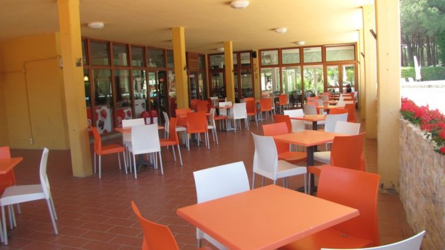 Un ristorante all'aperto con tavoli arancioni e bianchi, circondato da colonne gialle.