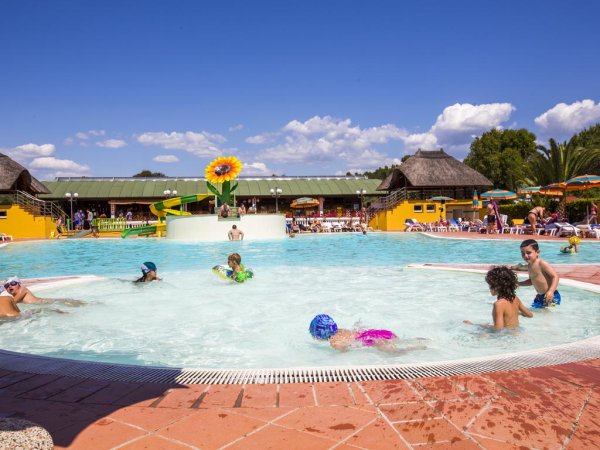 Bambini che giocano in una piscina poco profonda con uno scivolo giallo e verde.