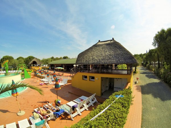 Piscina con lettini, ombrelloni colorati e un edificio giallo con tetto di paglia.