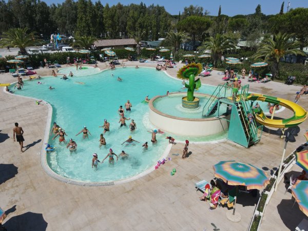 Piscina affollata con scivolo giallo e ombrelloni.