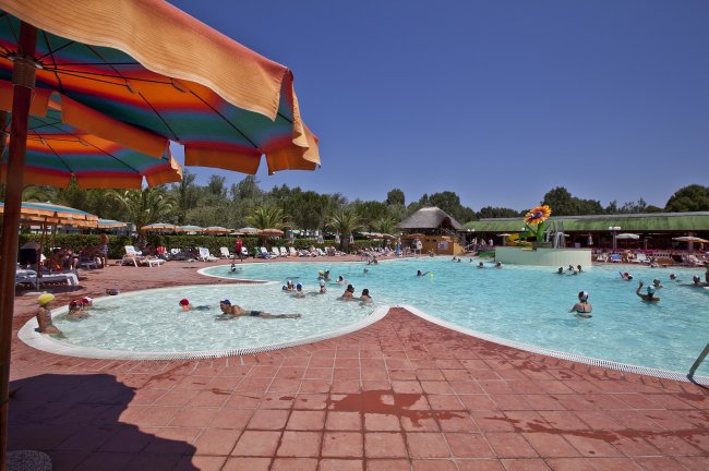 Piscina all'aperto con ombrelloni colorati e bagnanti in una giornata di sole.