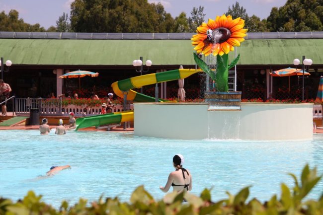 Piscina con scivoli colorati e decorazione gigante a forma di girasole.