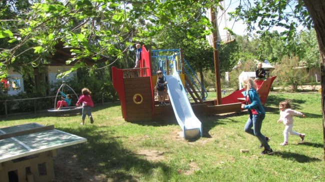 Bambini giocano in un parco con scivolo a forma di nave e altalene.