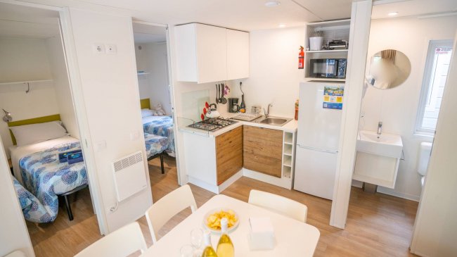 Un'area soggiorno e cucina di una casa mobile con tavolo da pranzo, frigorifero, lavabo e fornelli.