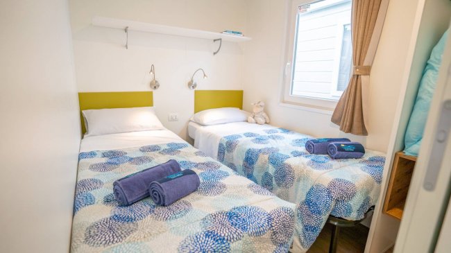 Una camera da letto con due letti singoli coperti da coperte blu e bianche, finestra e mensola.