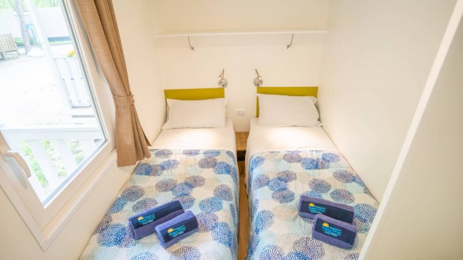 Due letti singoli affiancati con coperte blu e bianche, finestra con tende marroni.