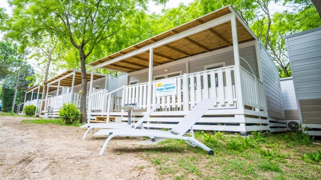 Strutture ricettive con veranda in legno e sdraio, circondate da alberi.