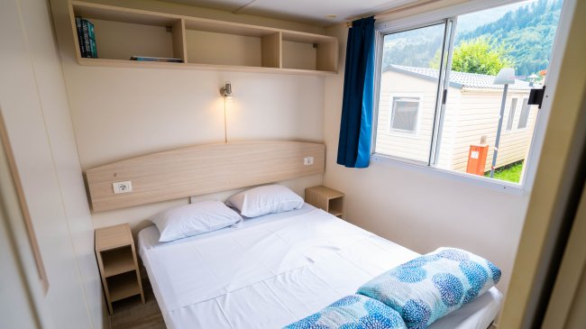 Camera da letto con letto matrimoniale, mensole, e finestra con tenda blu.