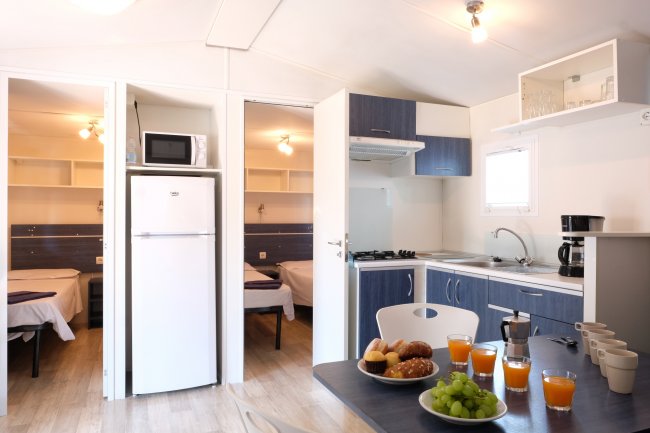 Cucina e zona pranzo con tavolo, frigo, e stoviglie, vicino a due stanze da letto.