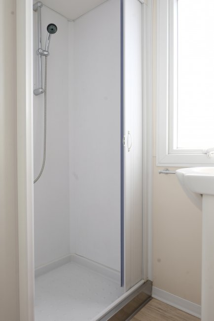 Cabina doccia bianca con porta scorrevole e finestra accanto.