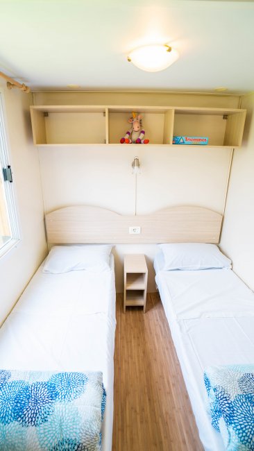 Due letti singoli con lenzuola bianche, mensola con peluche e libro.