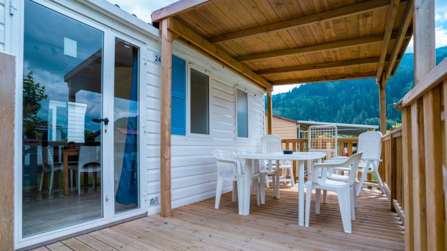 Terrazza con tavolo e sedie bianche, coperta da tettoia in legno.