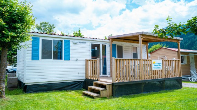 Casa mobile bianca con veranda in legno, circondata da prato verde.