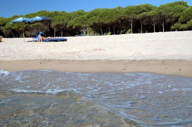 Spiaggia con ombrelloni blu, persona su lettino e mare calmo in primo piano.