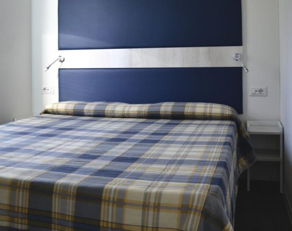 Letto matrimoniale con copriletto a quadri e testiera blu.