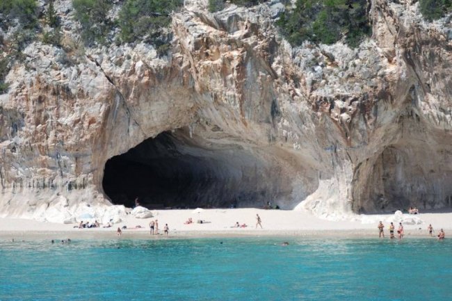 Spiaggia con grotte e persone, acqua azzurra.