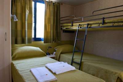 Stanza con un letto singolo e un letto a castello, lenzuola verdi e finestra con tende verdi.
