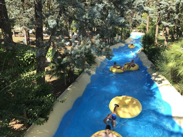 Persone su ciambelle gialle in un fiume lento circondato da alberi.