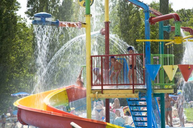 Bambini sotto spruzzi d'acqua e scivolo colorato.