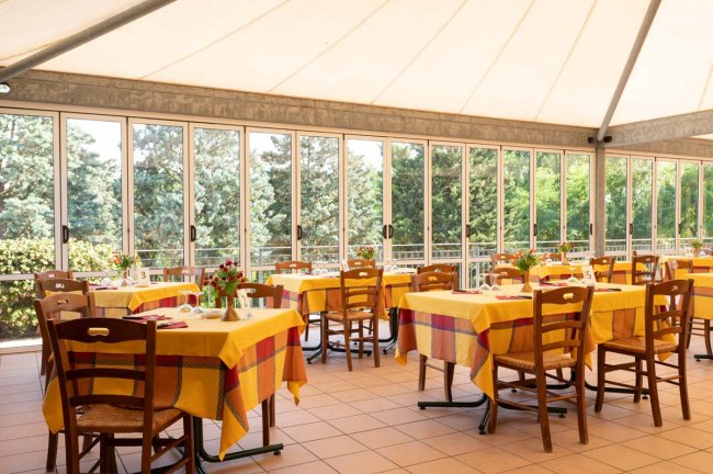 Sala da pranzo con vetrate e tavoli gialli.