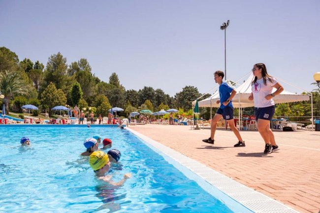 Istruttori camminano vicino a piscina con nuotatori.