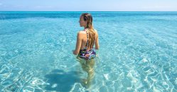 Una persona in costume entra in acqua cristallina con l'orizzonte azzurro in lontananza.