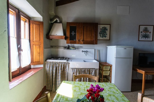 Cucina con tavolo verde, lavello e finestra soleggiata.