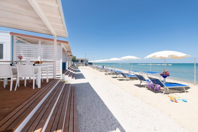 Passerella di legno lungo una spiaggia con lettini.