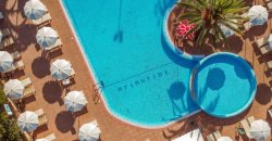 Una spiaggia sabbiosa con mare calmo e una roccia in lontananza sotto un cielo azzurro.