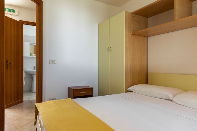 Letto matrimoniale con copriletto giallo, armadio e comodino.