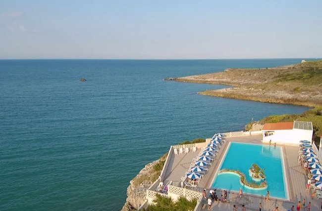 Piscina panoramica su scogliere con vista mare e ombrelloni blu.