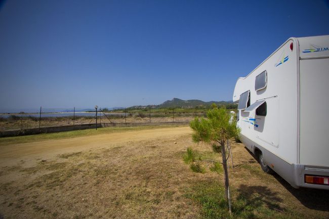 Un camper parcheggiato su un prato con vista su una recinzione e colline in lontananza.