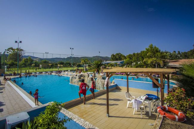 Una piscina all'aperto con bagnini e una zona relax con tavoli e sedie sotto un pergolato.