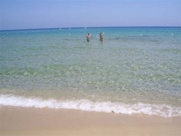 Una spiaggia sabbiosa con mare limpido, due persone camminano in acqua.