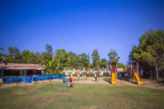 Un parco giochi con scivoli colorati, bambini che giocano e tavoli blu sullo sfondo.