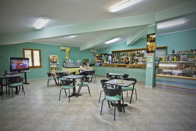 Ampia sala con tavoli e sedie, bancone bar e televisore in un angolo.