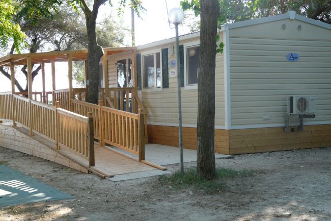 Casa mobile con rampa di legno accessibile, circondata da alberi.