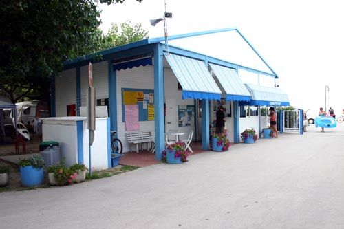 Edificio bianco e blu, con piante e cartelli, su strada asfaltata.