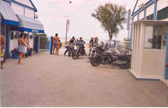 Motociclette parcheggiate vicino all'ingresso di un'area turistica con persone in costume da bagno.
