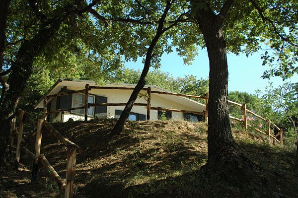 Struttura in cima a una collina, circondata da alberi e staccionata.