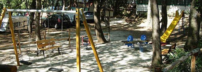 Parco giochi con altalene, scivolo e dondoli tra gli alberi.