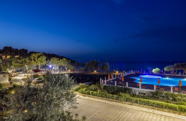 Vista notturna di una piscina illuminata e giardini.