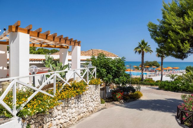 Struttura con pergolato, giardino fiorito e vista sulla piscina e sul mare.